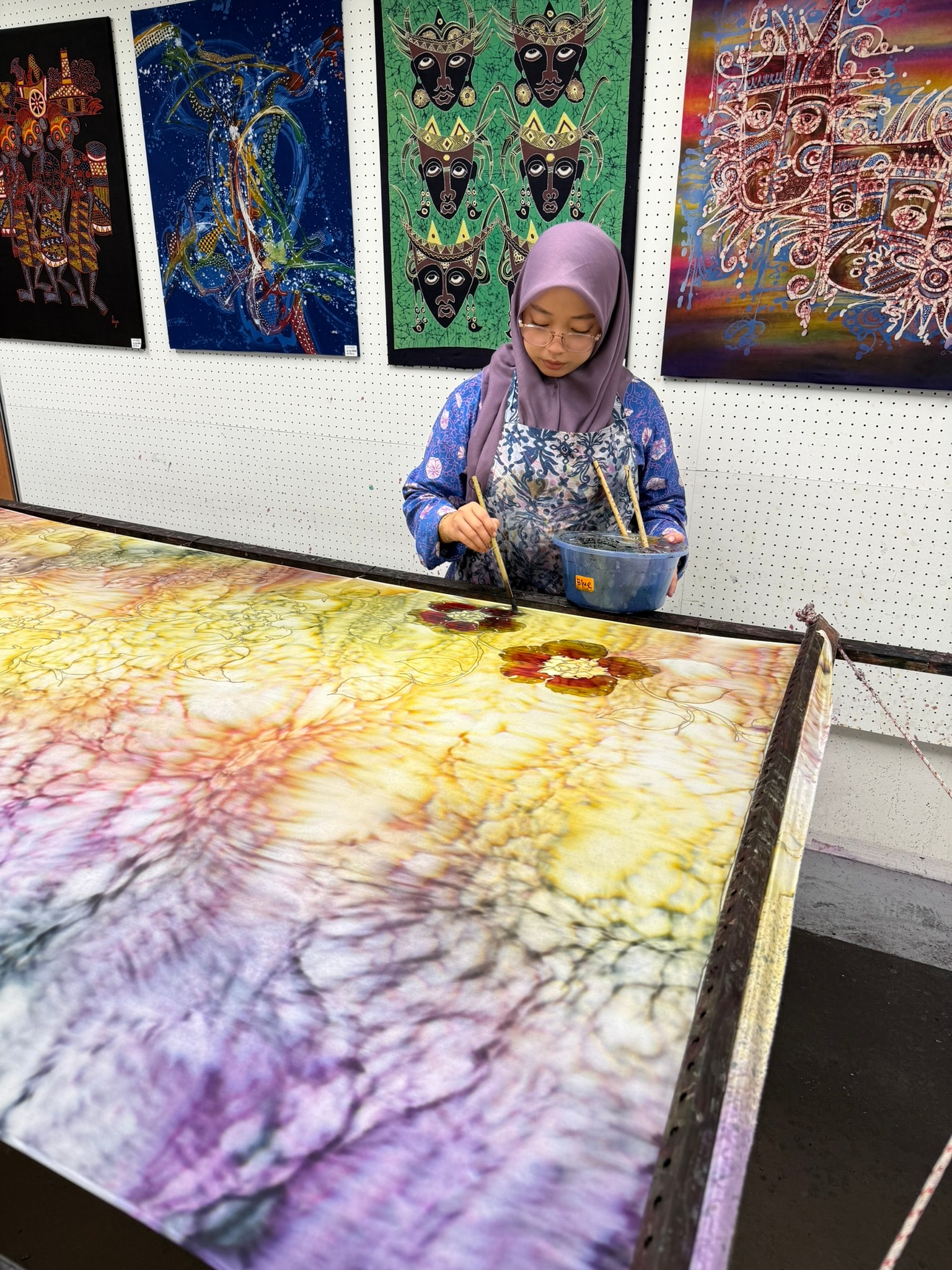 Batik artist carefully applying color to a large piece of fabric
