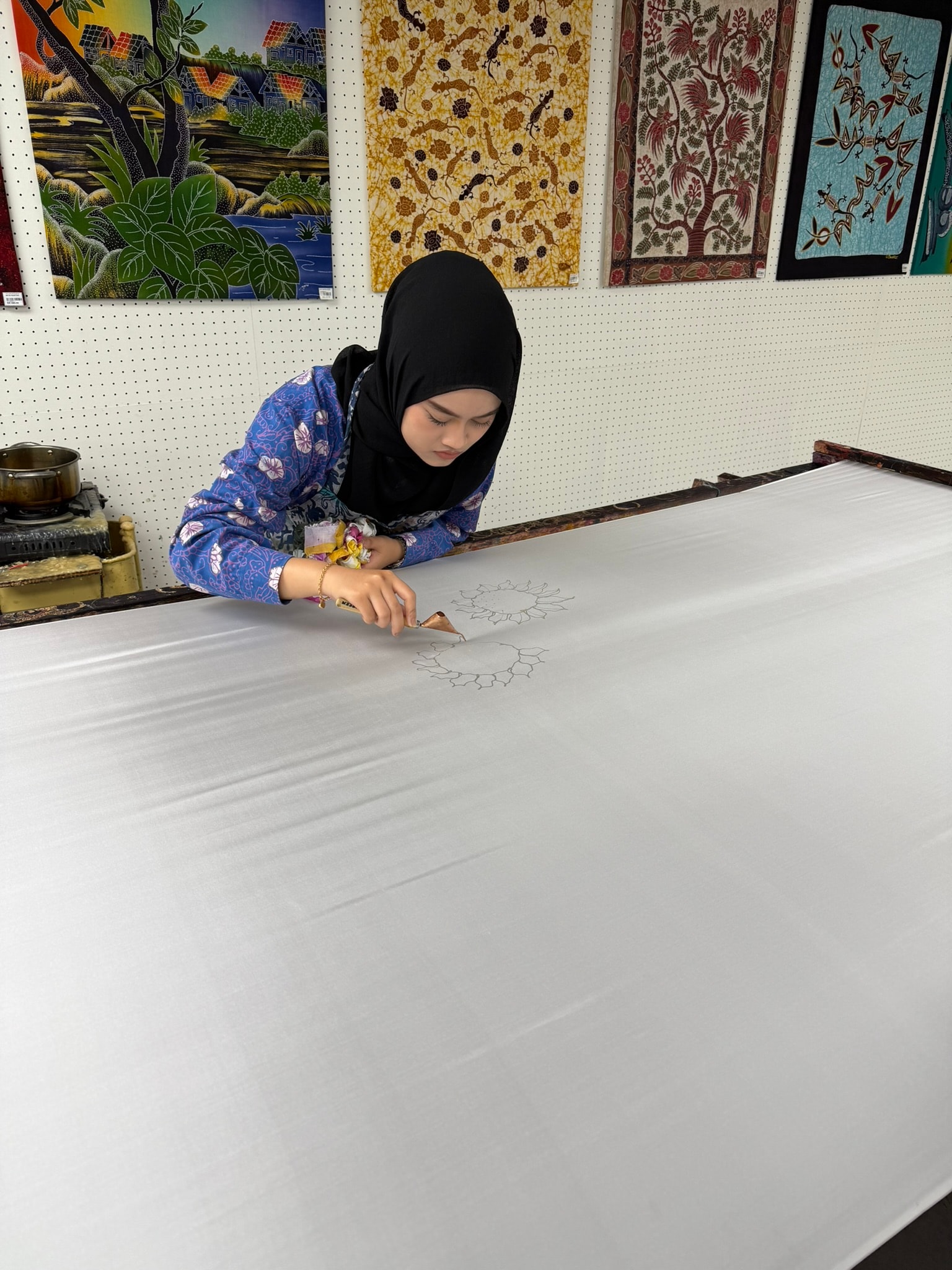 Batik artist using a wax tool to draw a design freehand onto a large piece of white fabric