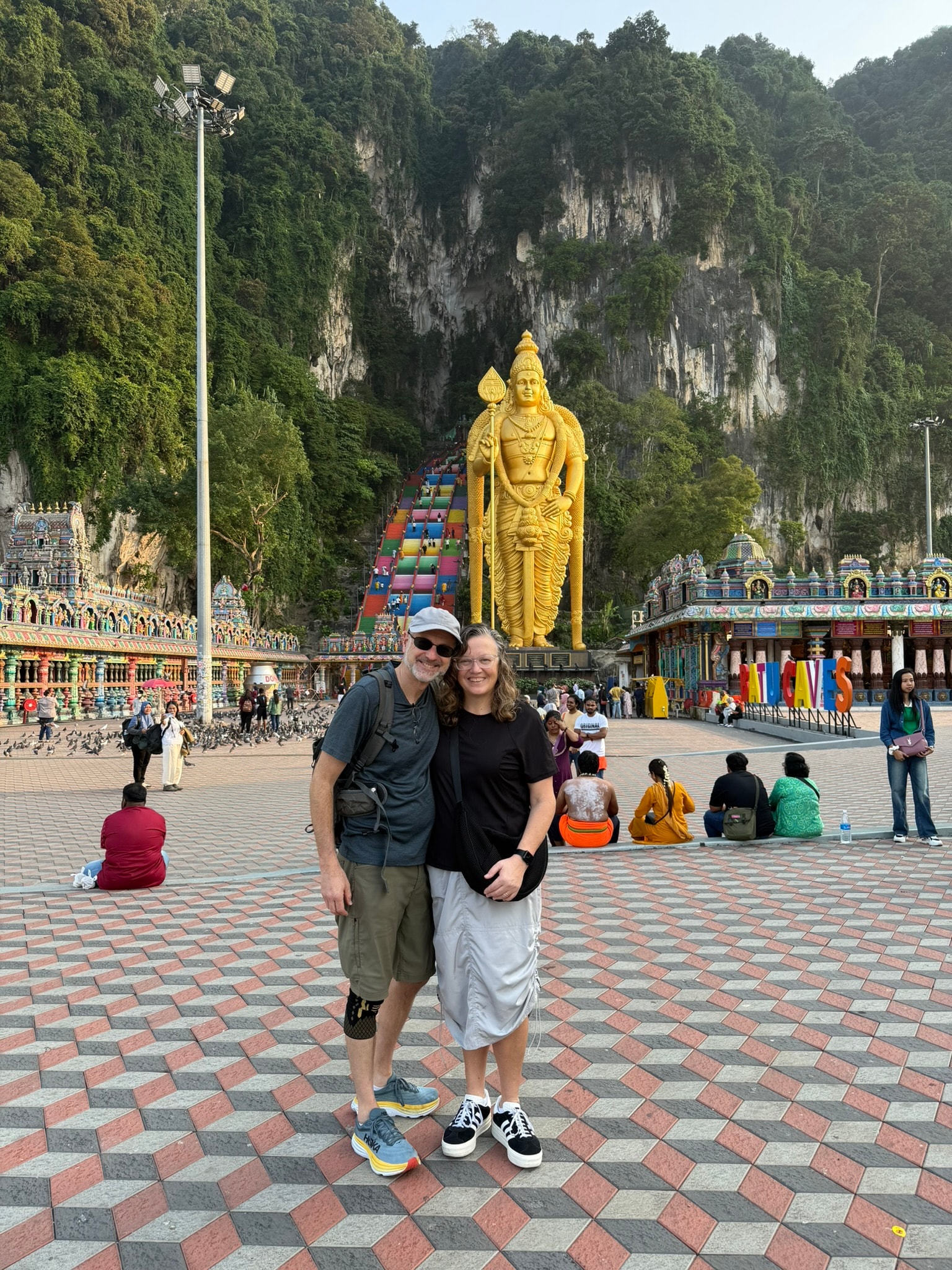 Cheryl and Steve at Batu Caves with the golden Murugan statue and colorful staircase behind them