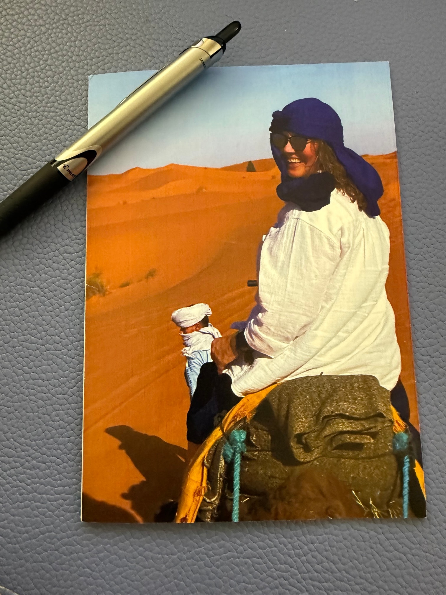 A printed photo of a woman riding a camel across orange Sahara dunes, sent by Debbie as a keepsake from the Morocco trip