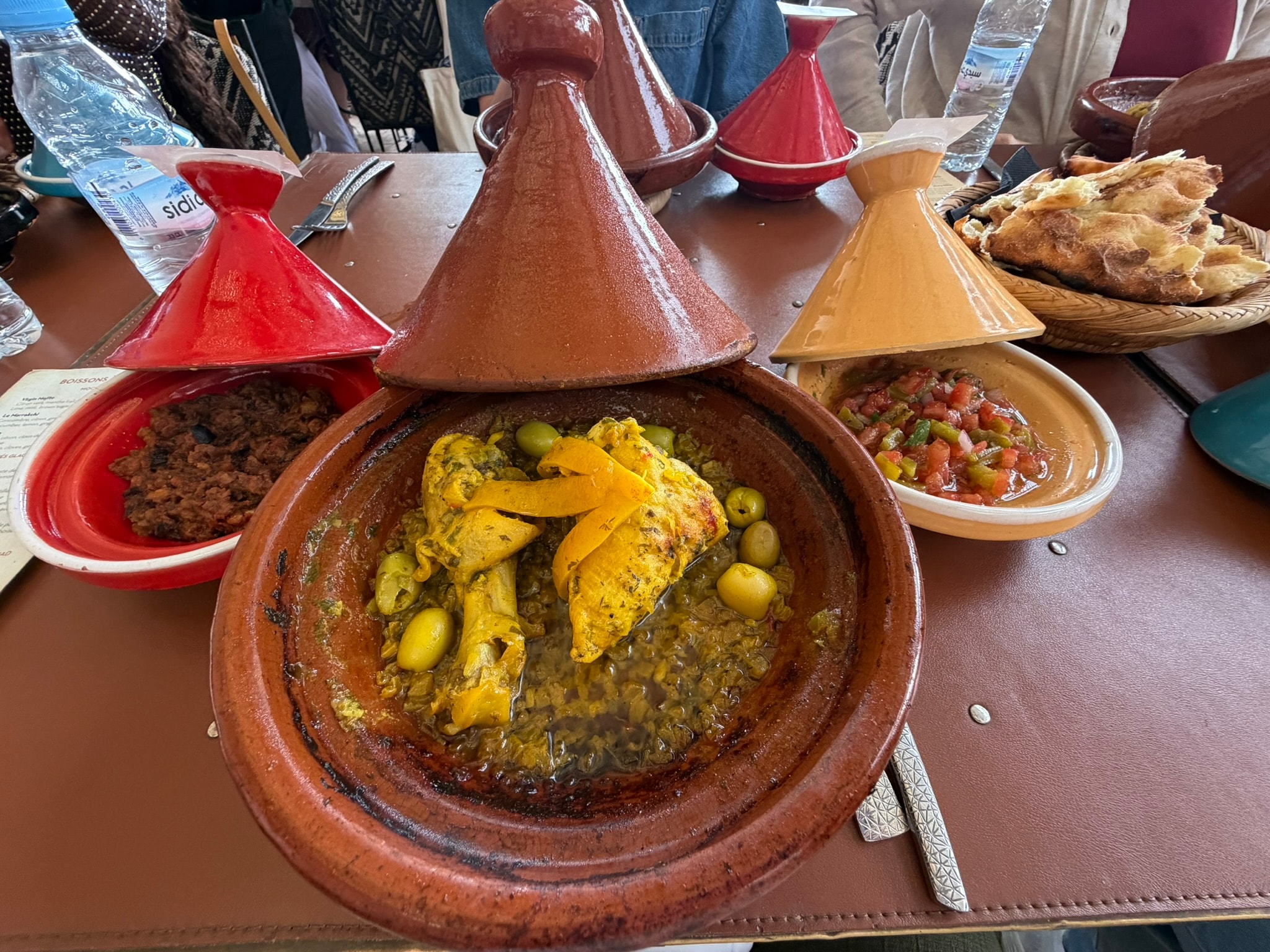 A spread of traditional Moroccan tagines — chicken with olives and preserved lemon, lamb, and fresh bread — served at a restaurant in Marrakech